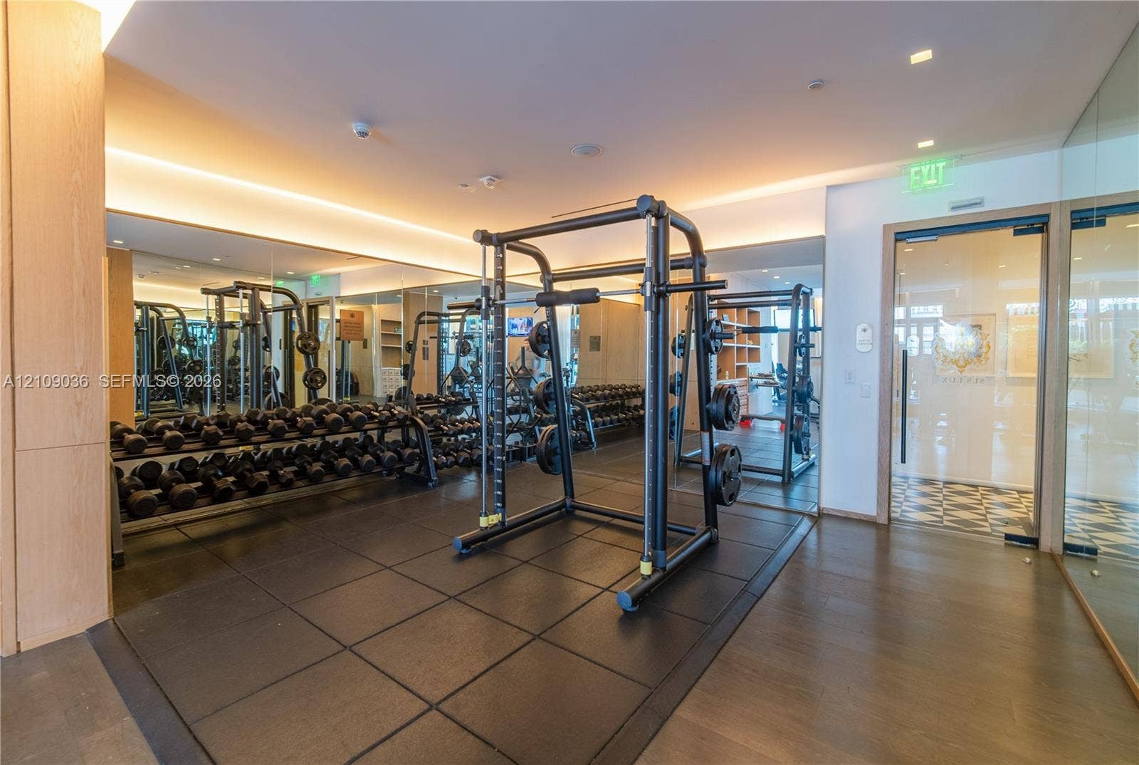 Fitness center featuring rubber flooring, recessed cove lighting, full-wall mirrors, wood-finish wall panels, and glass-entry doors