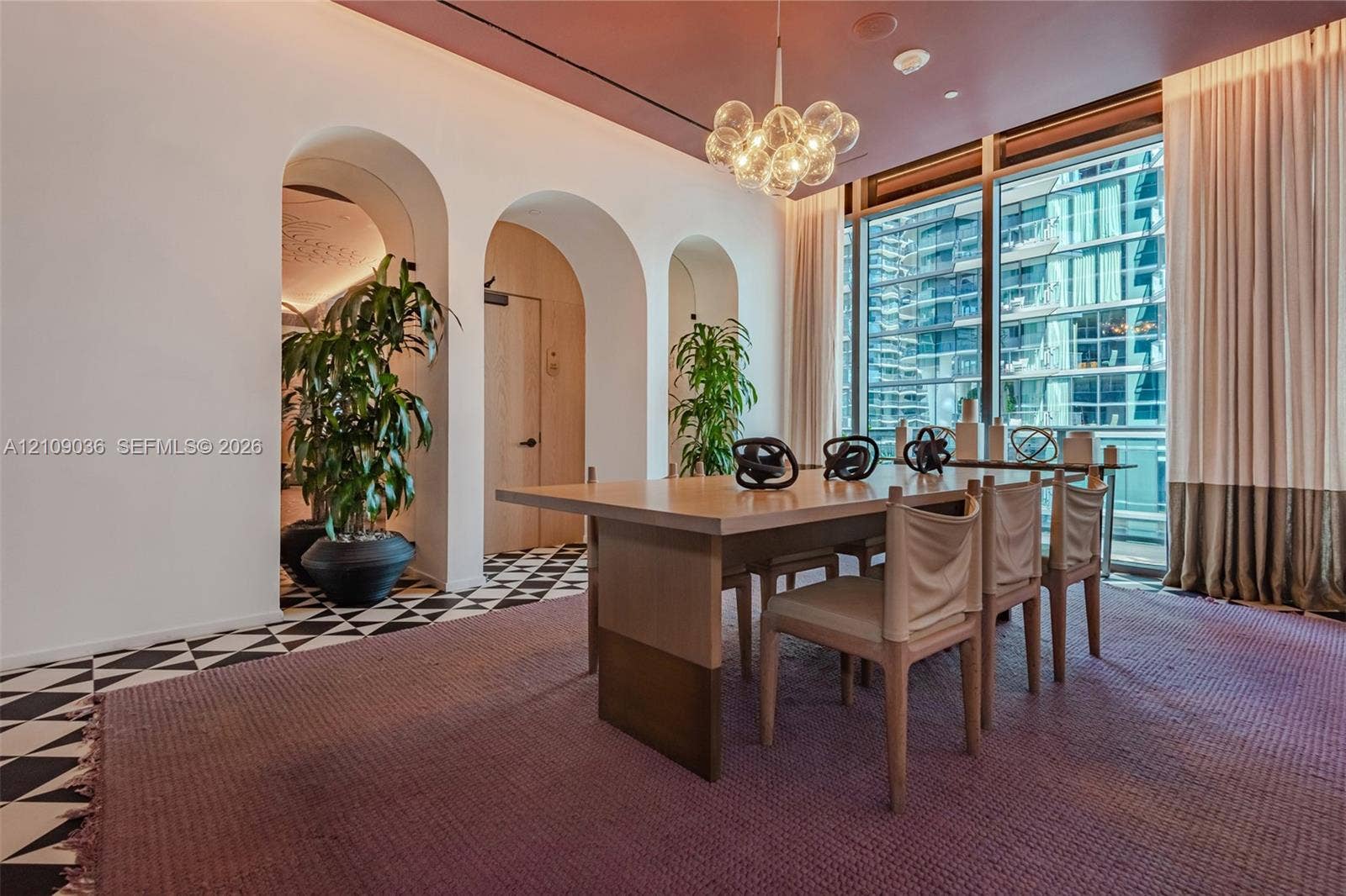 Architectural arched entryways, floor-to-ceiling windows with full-height drapery, geometric pattern tile flooring, and a multi-globe glass pendant light fixture