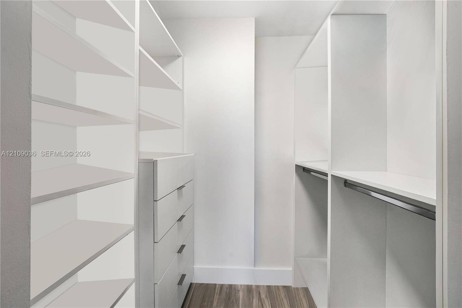 Walk-in closet featuring white built-in shelving, integrated dresser drawers with bar pulls, and a metal hanging rod over wood-finish flooring
