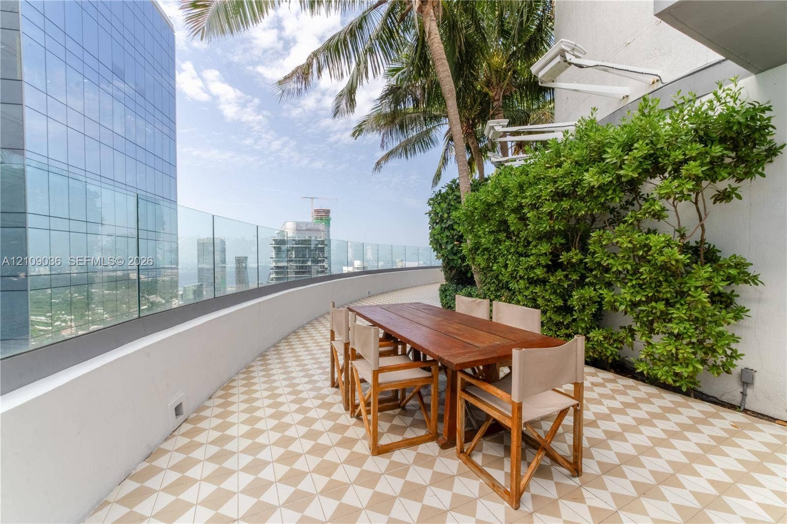 Expansive terrace featuring a glass panel railing, patterned tile flooring, mature landscaping, and building-integrated lighting