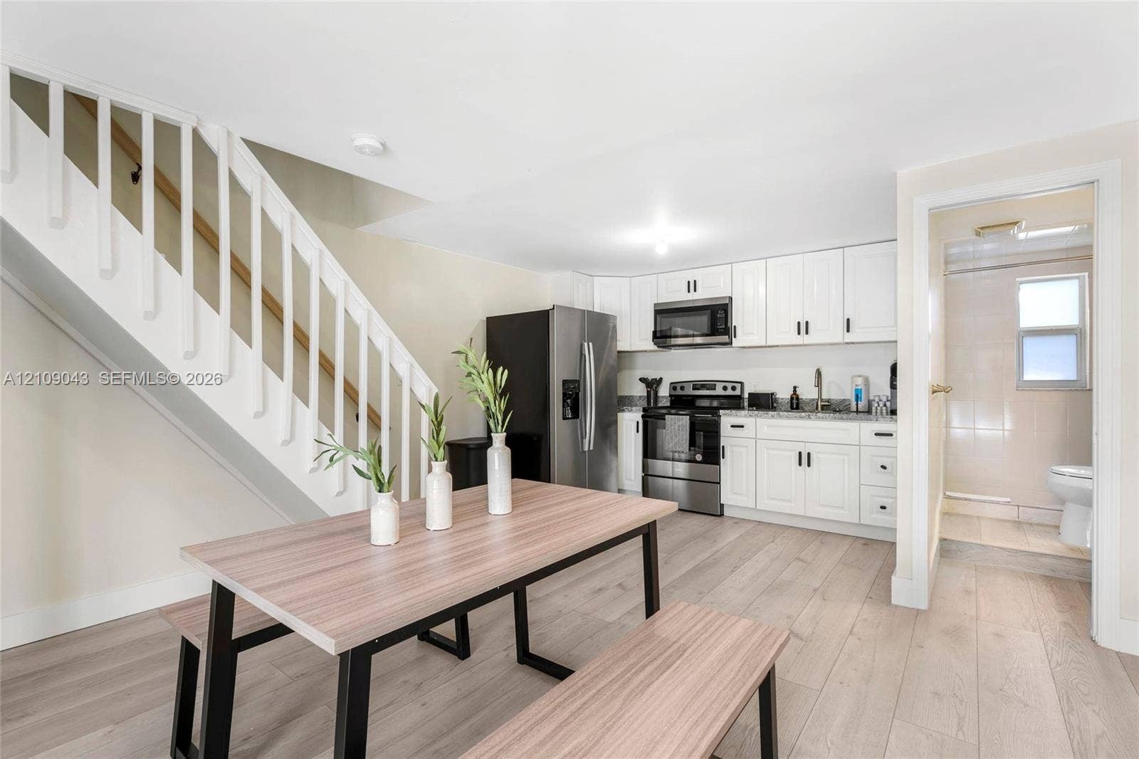 605 SW 17th Street, #1-3, Fort Lauderdale, Fort Lauderdale, FL 33315 Kitchen area featuring white Shaker-style cabinetry, stainless steel appliances, wood-finish flooring, and a white staircase with a wooden handrail