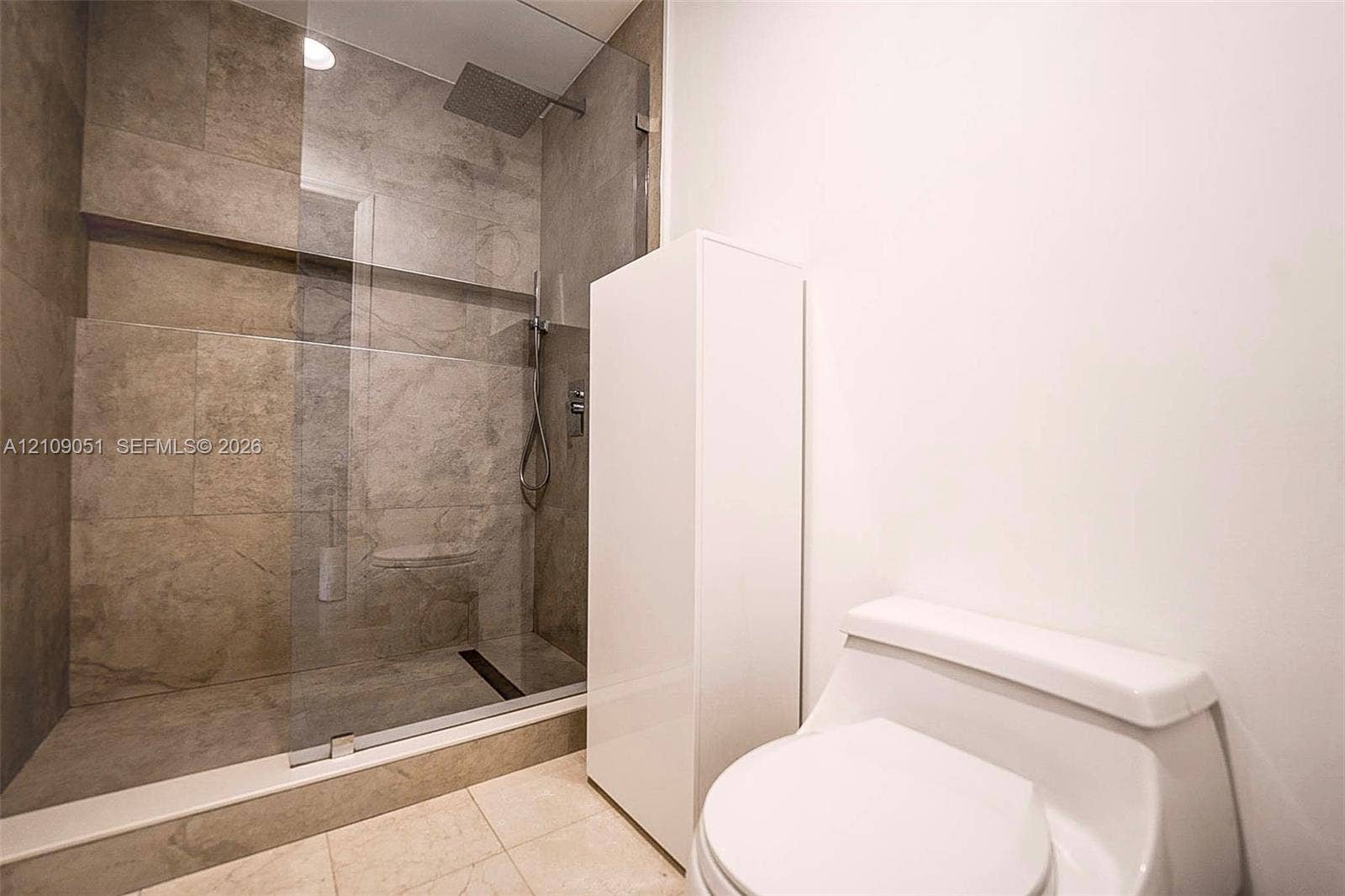 Walk-in shower featuring oversized stone-finish wall tiles, a built-in recessed shelf, a frameless glass enclosure, and a ceiling-mounted rainfall showerhead
