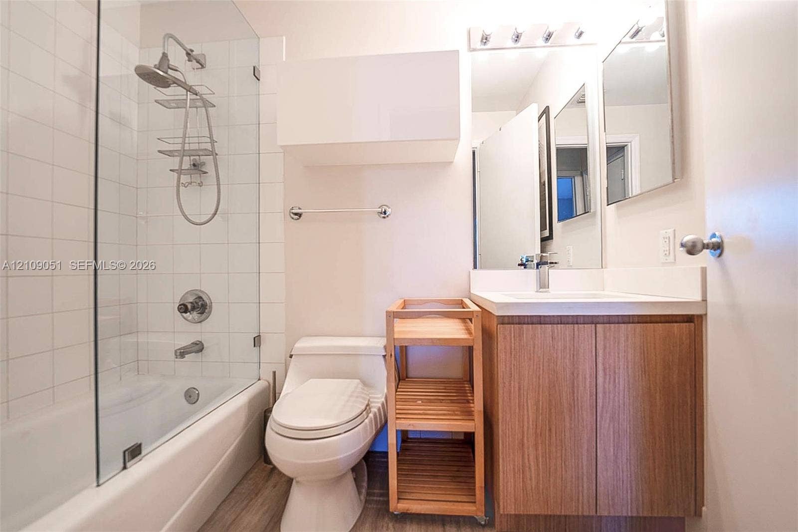 Bathroom featuring a wood-finish vanity with a white countertop, glass-enclosed shower, wall-mounted cabinet, and large-format mirror with integrated lighting