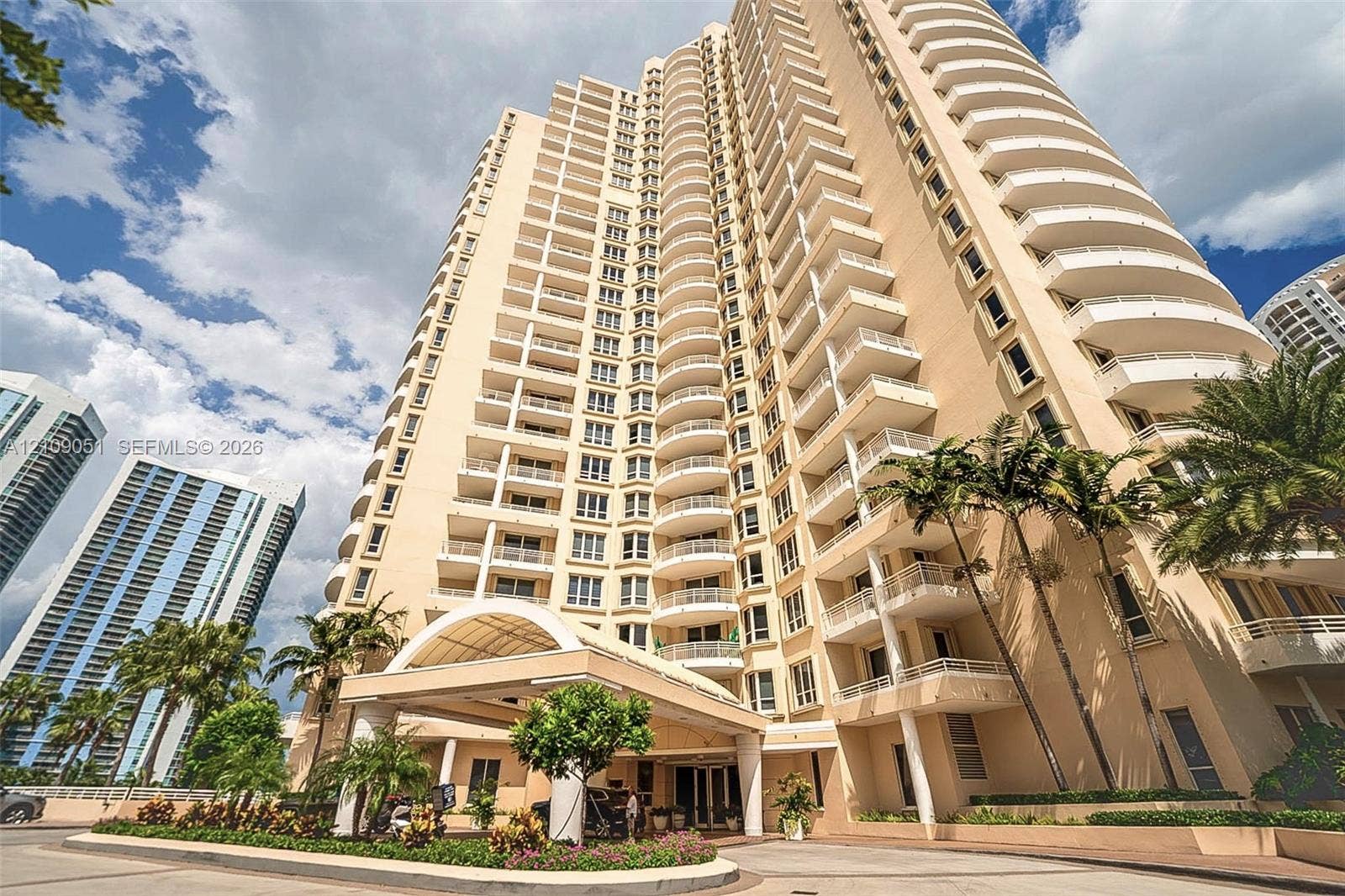 High-rise exterior featuring curved balconies, a covered entrance porte-cochre, and manicured landscaping
