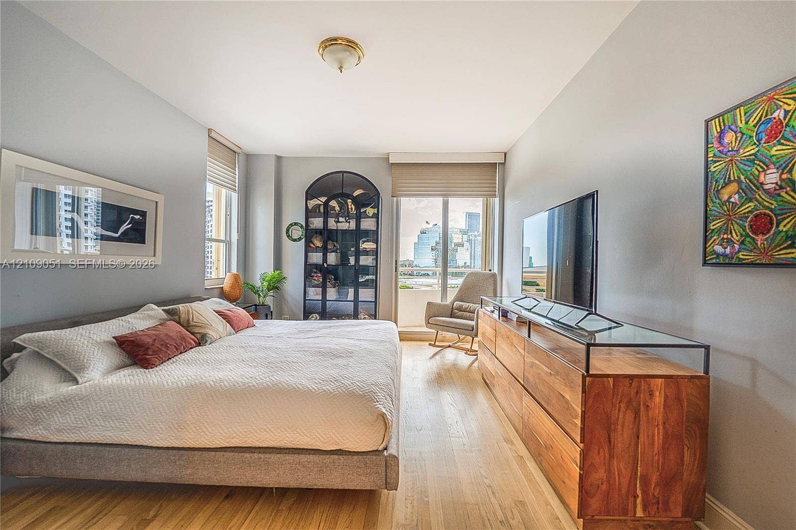 Wood-finish flooring, built-in arched display cabinetry with glass shelving, large-format windows with custom shades, and a glass-paneled entry door