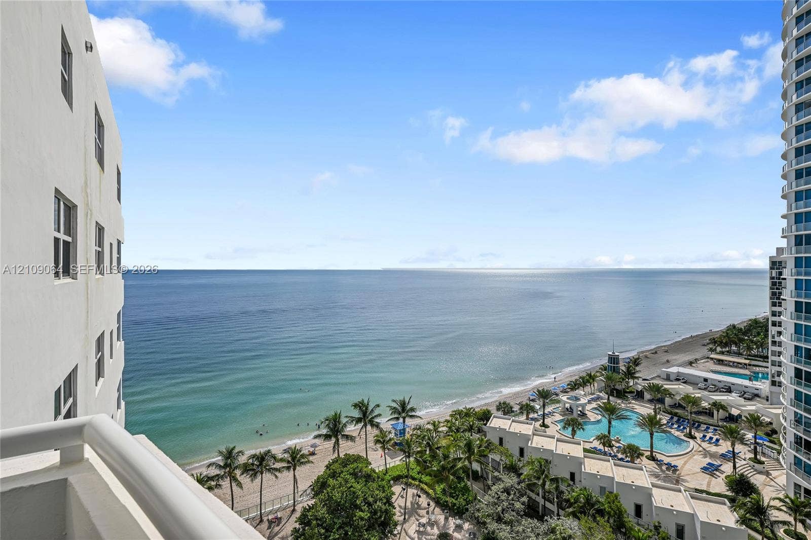 High-rise balcony overlooking the ocean and coastline, featuring structural railings and proximity to resort-style pools and sandy beaches