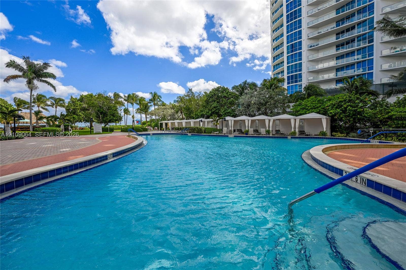 Resort-style pool featuring a contoured basin, paved sun deck, submerged entry steps, and poolside cabanas