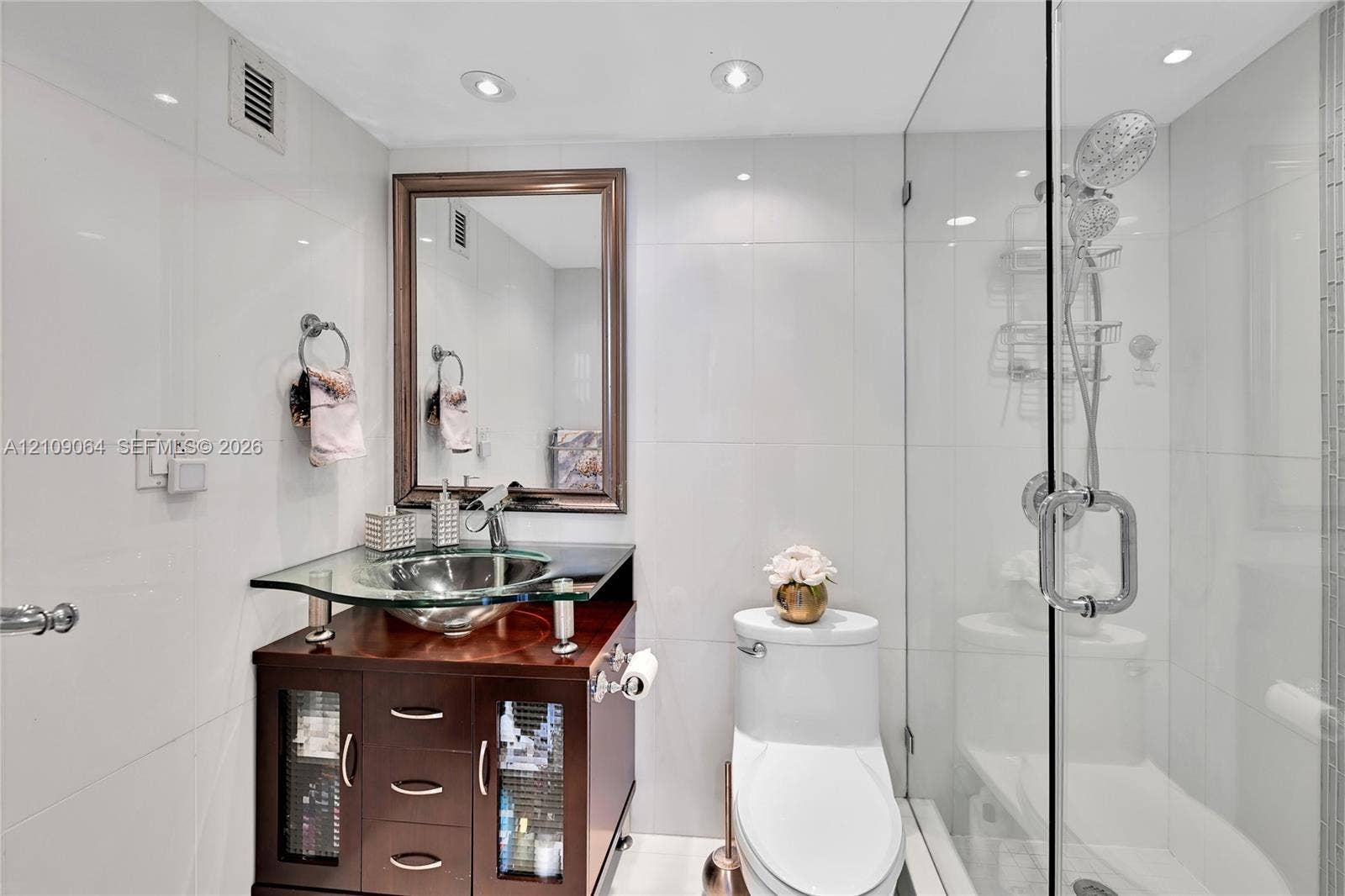Dark wood-finish vanity with a glass countertop, integrated vessel sink, frameless glass shower enclosure, and recessed lighting