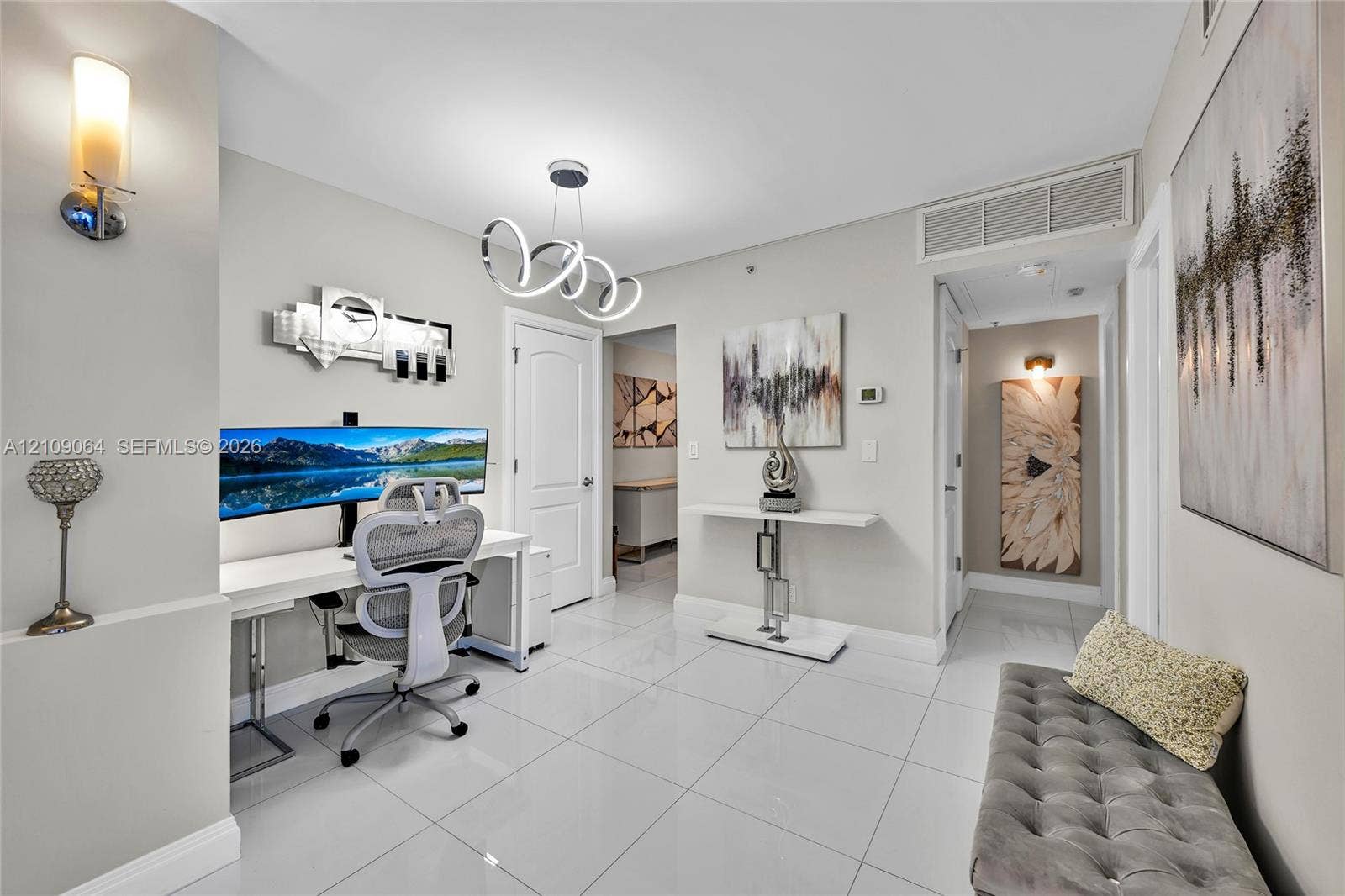 Open-concept space featuring polished tile flooring, a modern multi-ring sculptural chandelier, wall-mounted ambient sconce lighting, and a built-in recessed storage niche