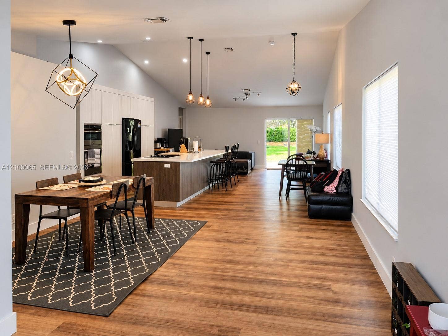 Vaulted ceilings, wood-finish flooring, kitchen island with stone countertop, recessed lighting, and geometric pendant fixtures