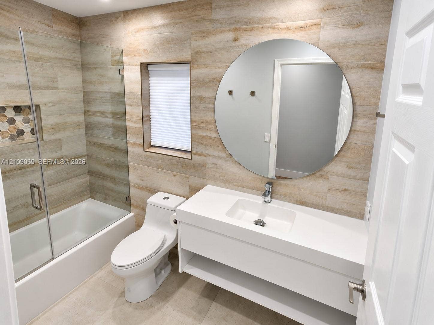Full-wall wood-finish tile cladding, floating vanity with integrated rectangular basin, frameless glass shower enclosure featuring a built-in recessed niche, and large circular mirror