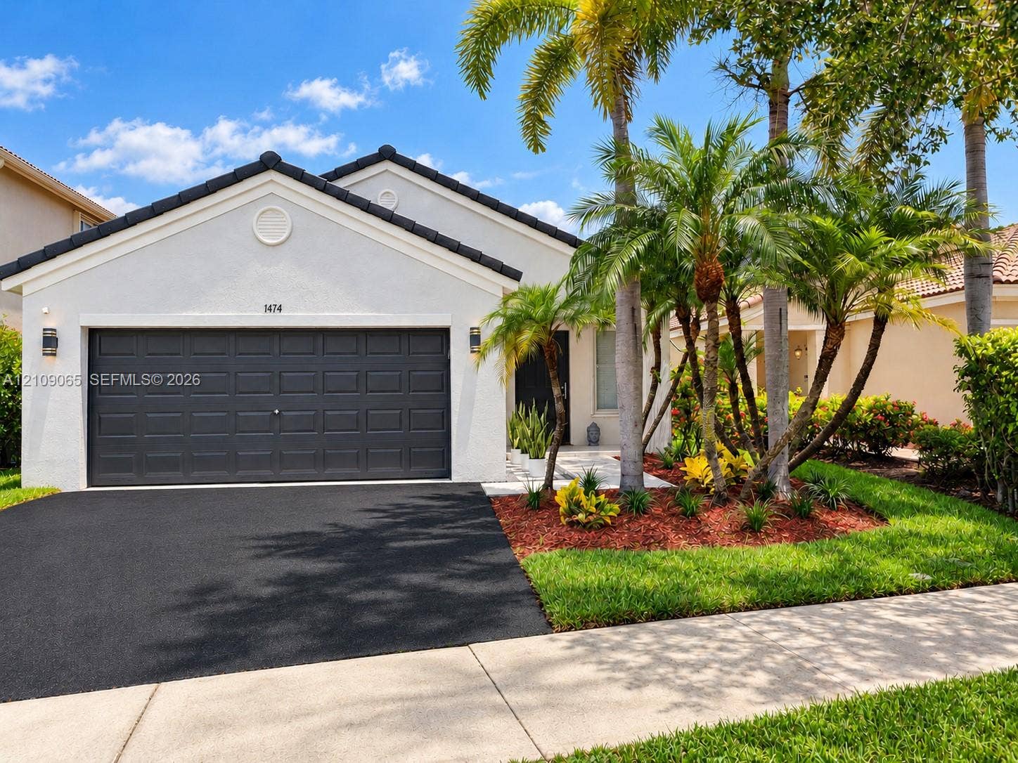 Stucco exterior with a tiled roof, asphalt driveway, two-car garage, and established palm landscaping