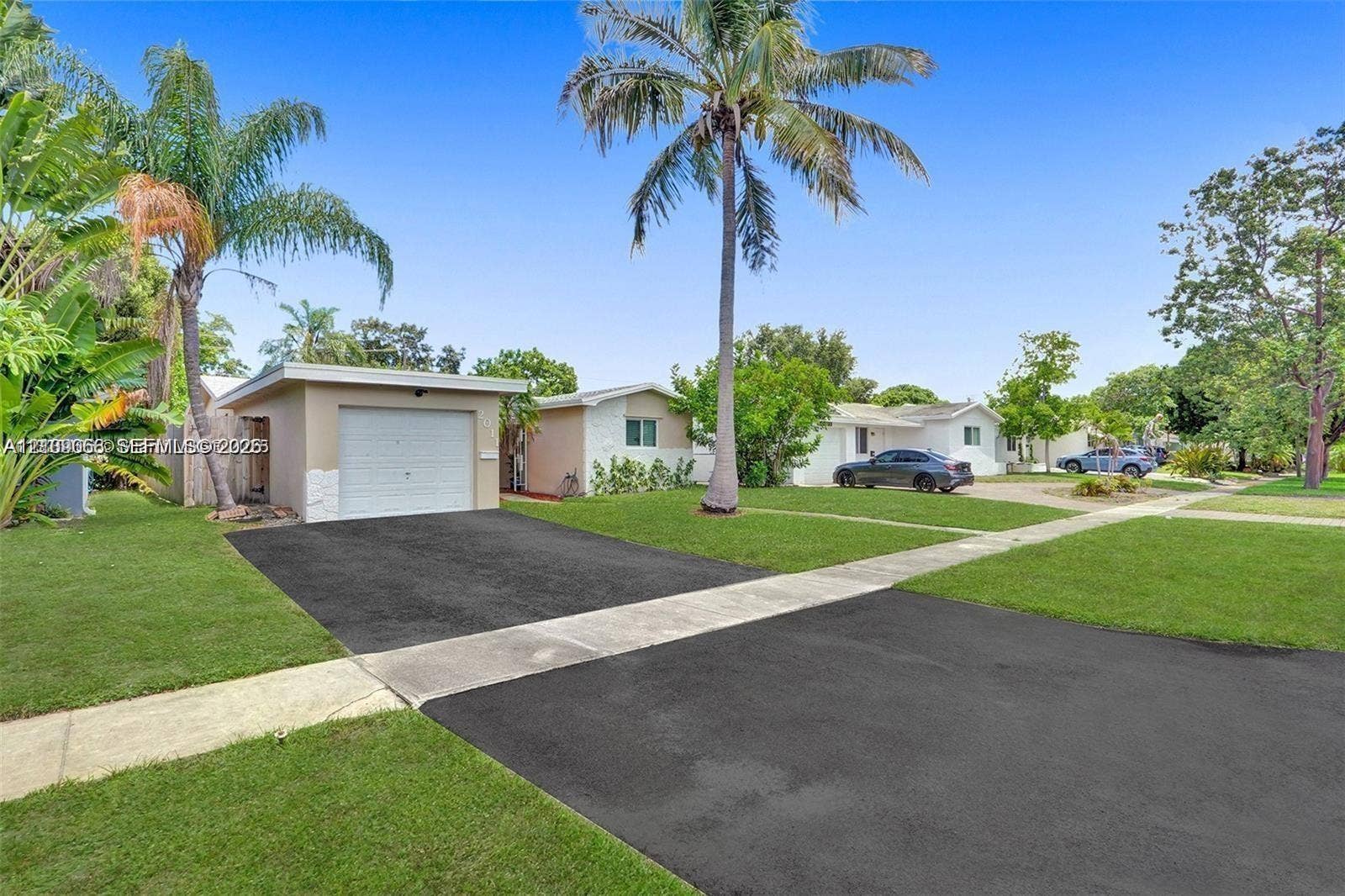 Single-story residence featuring a paved driveway, attached garage, stone facade accents, and mature palm trees
