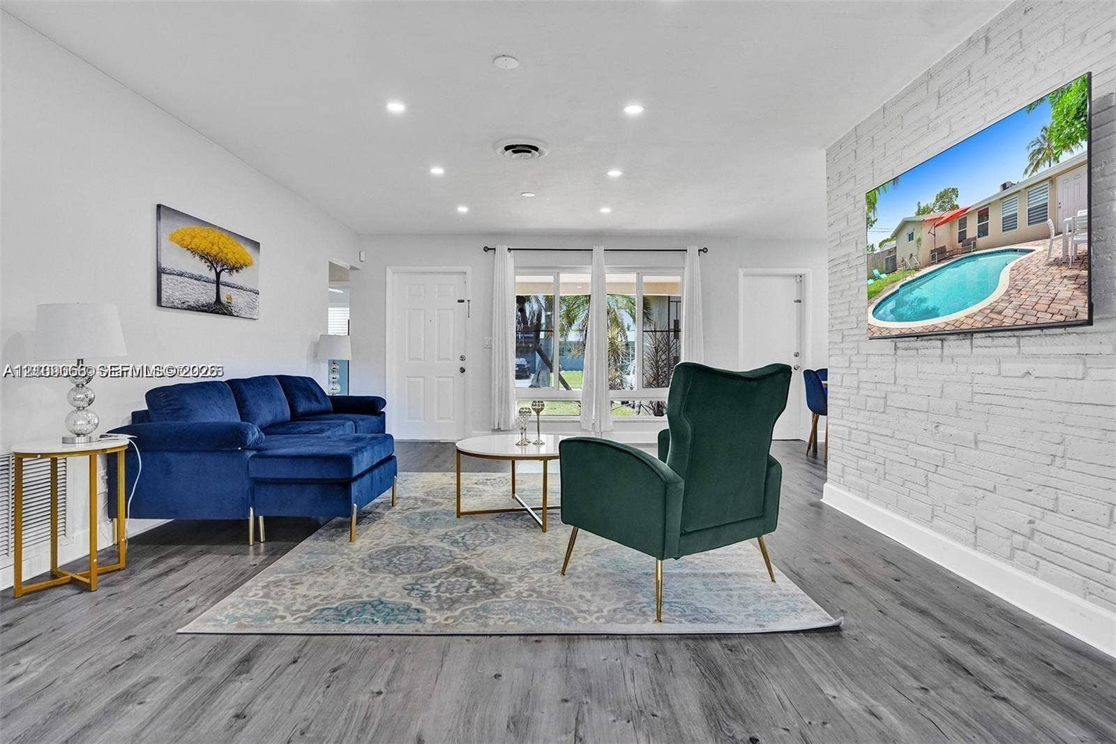 Open-concept living space featuring wood-finish flooring, recessed lighting, and a prominent white painted brick accent wall