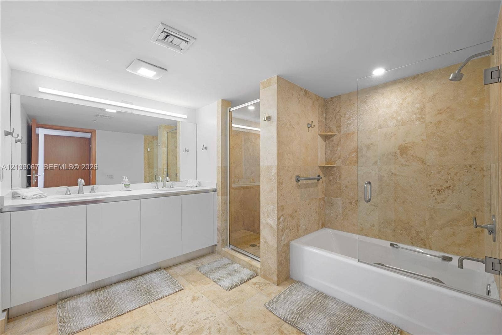Double vanity with rectangular sinks, expansive wall-to-wall mirror, tiled soaking tub with glass partition, and separate walk-in shower featuring natural stone wall tile