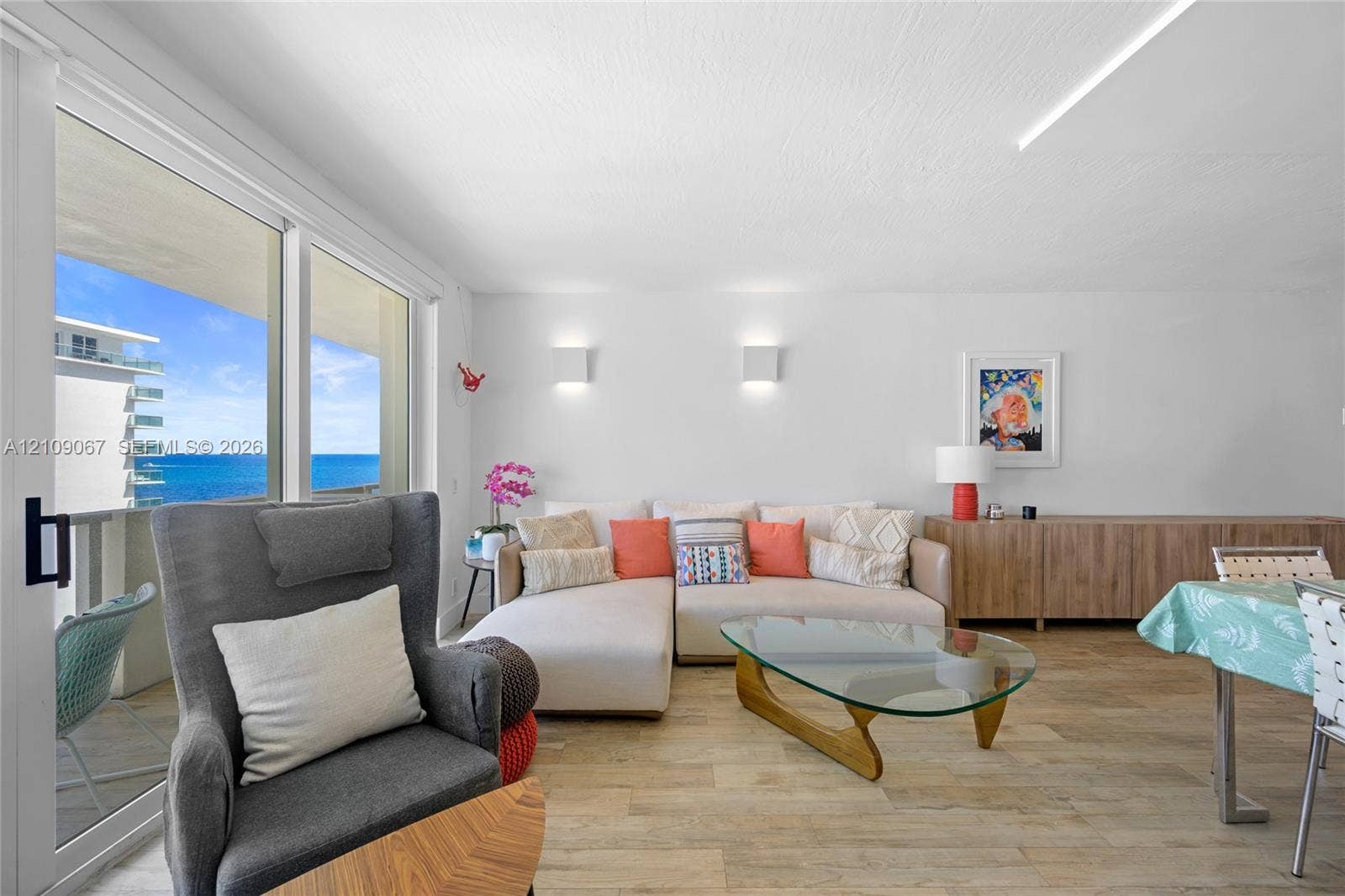 Living area featuring wood-finish flooring, floor-to-ceiling sliding glass doors, wall-mounted light fixtures, and expansive ocean and coastal scenery