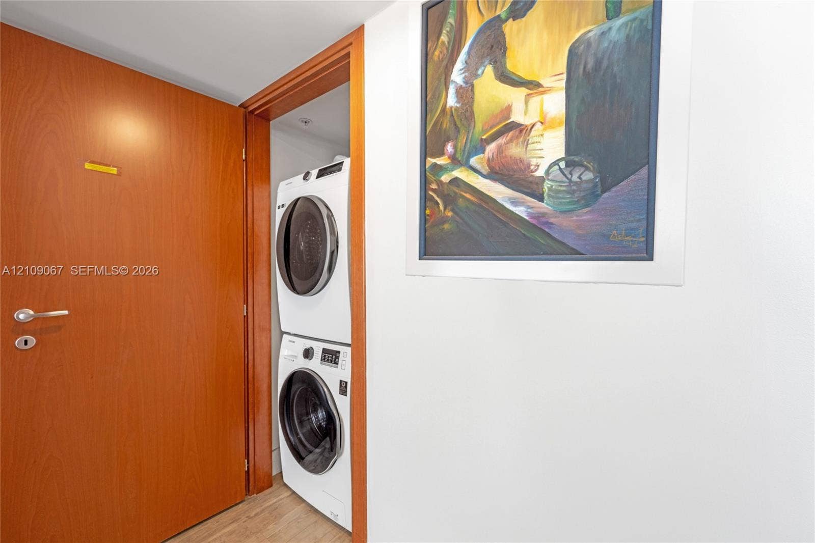Laundry alcove featuring a stacked white washer and dryer unit, wood-finish interior door, and door frame with natural wood trim