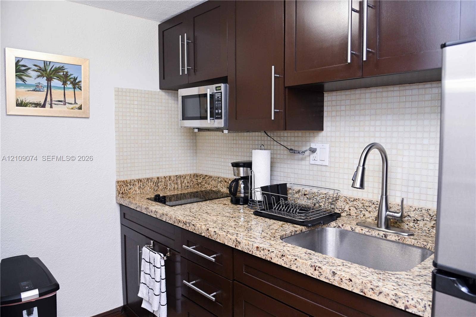 Kitchen featuring dark-finish cabinetry, stone-surface countertops, mosaic tile backsplash, stainless steel sink with pull-down faucet, and built-in microwave