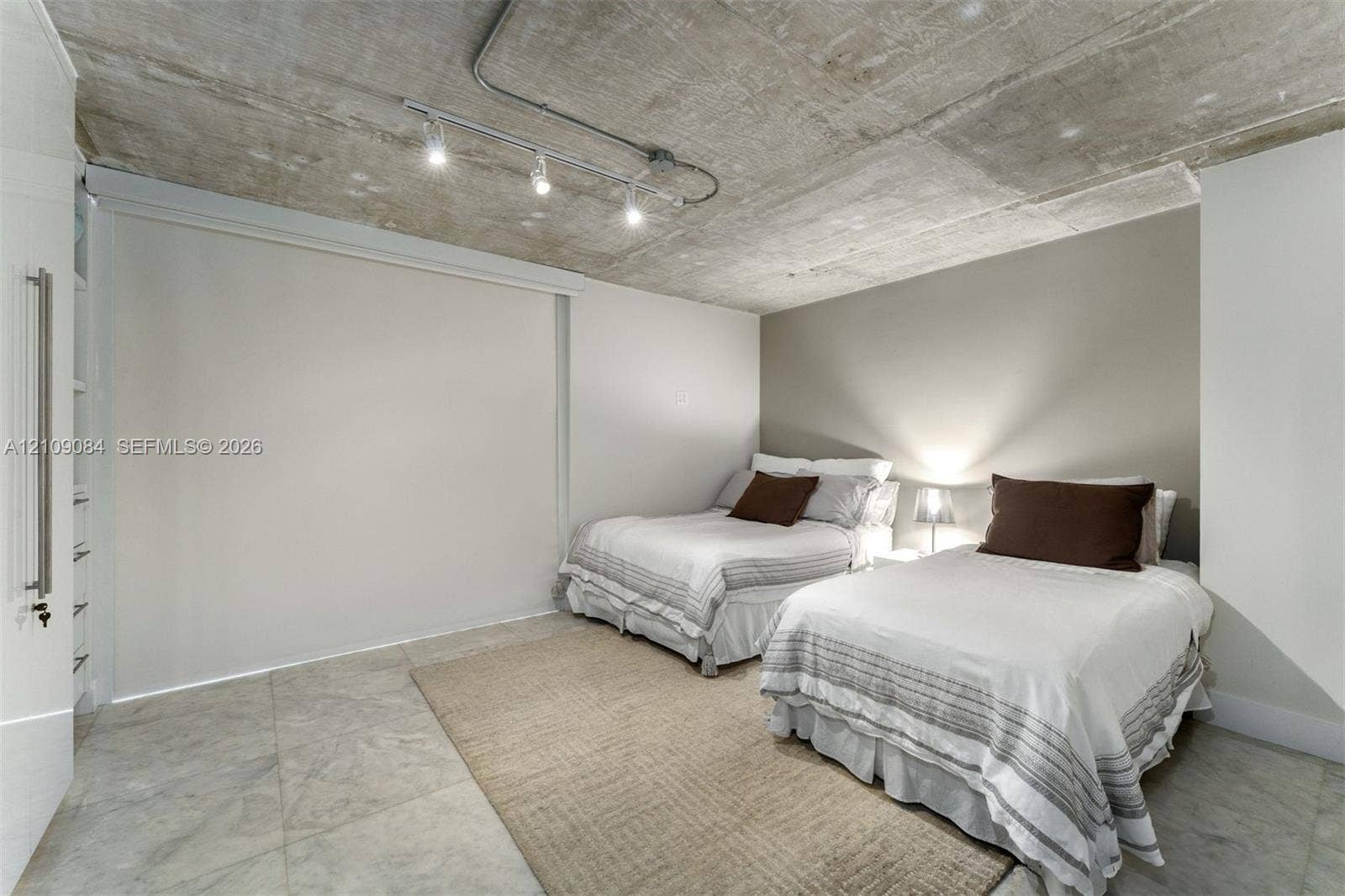 Exposed concrete ceiling with industrial-style track lighting, large-format tile flooring, and custom built-in floor-to-ceiling storage cabinetry