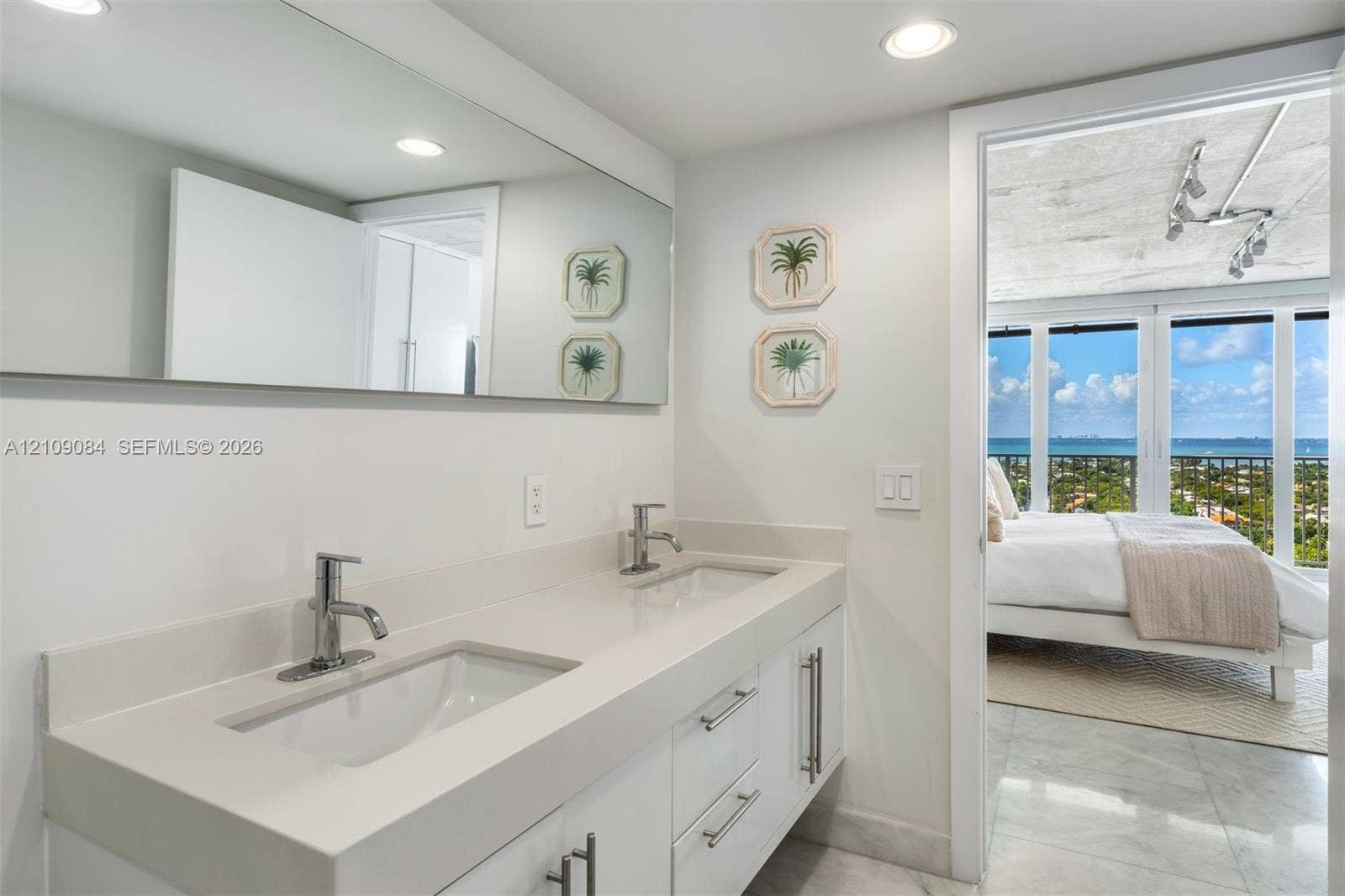 Bathroom featuring a double-sink vanity with a solid-surface countertop, full-width wall mirror, and polished chrome fixtures, finished with stone flooring