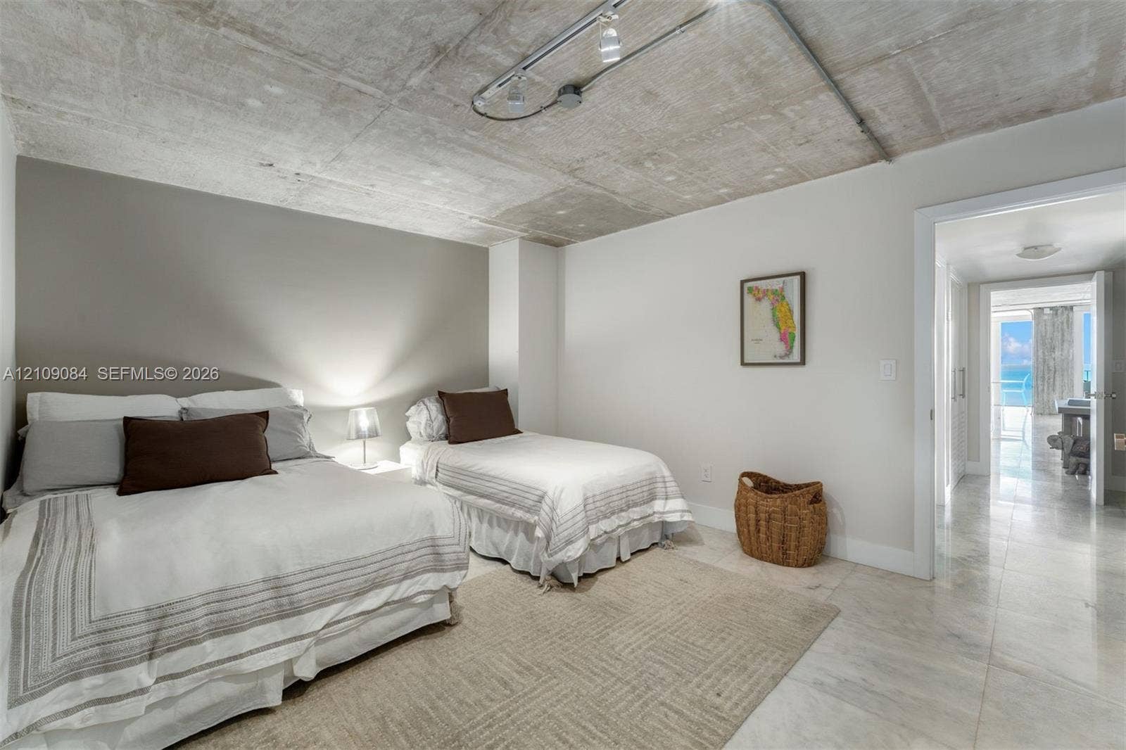 Exposed concrete ceiling with industrial track lighting, neutral wall finishes, and polished stone tile flooring