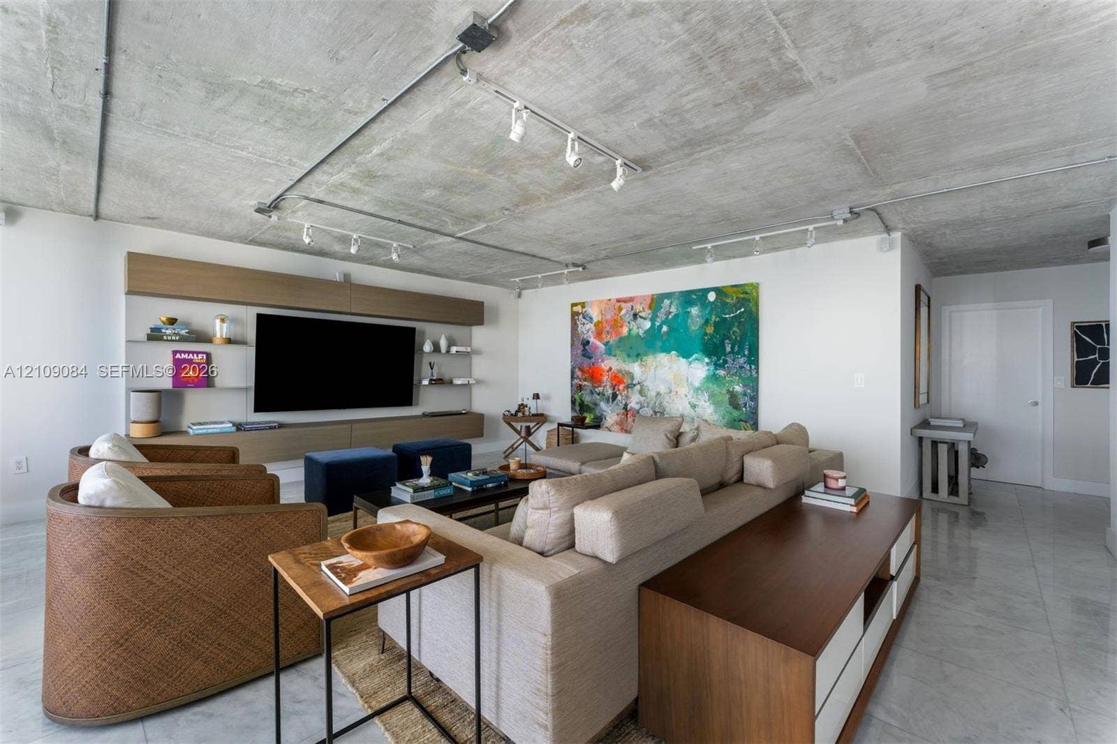 Exposed concrete ceiling with industrial-style track lighting, large-format tile flooring, and custom wall-mounted wood cabinetry with integrated shelving