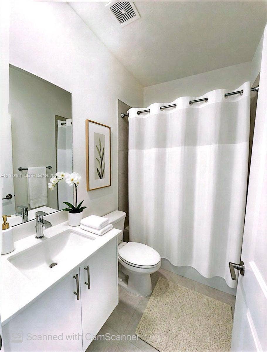 Bathroom featuring a white vanity cabinet, solid-surface countertop with an integrated sink, polished chrome faucet, full-width wall mirror, and a tile-surround shower