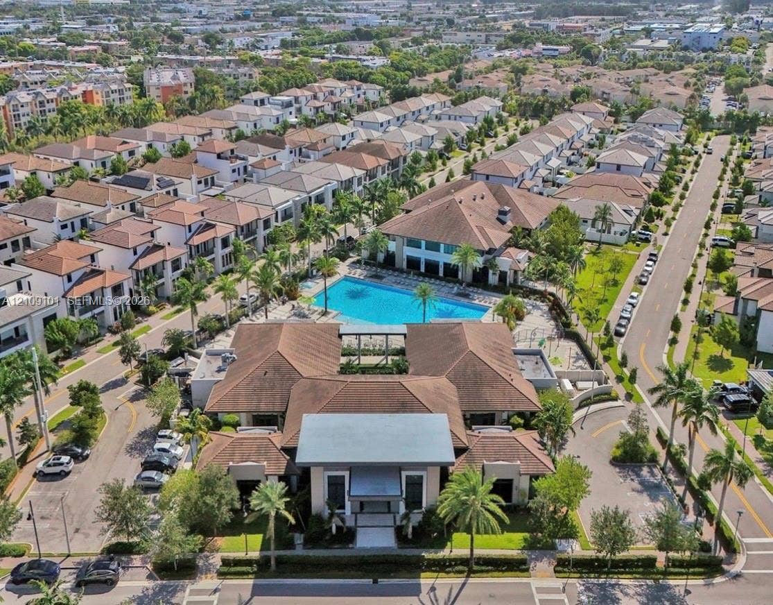 Aerial perspective of a community facility featuring a large swimming pool, multi-hipped rooflines, paved parking areas, and manicured landscaping