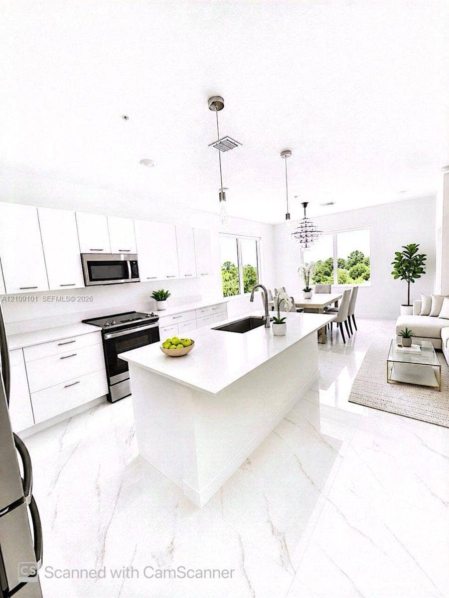 Kitchen featuring white flat-panel cabinetry, quartz countertops, central island with an undermount sink, stainless steel appliance suite, and large-format tile flooring