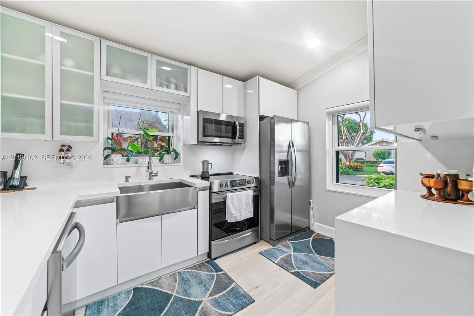 Kitchen featuring white flat-panel cabinetry with glass-front uppers, stainless steel apron-front sink, stone-finish countertops, and matching stainless steel appliances