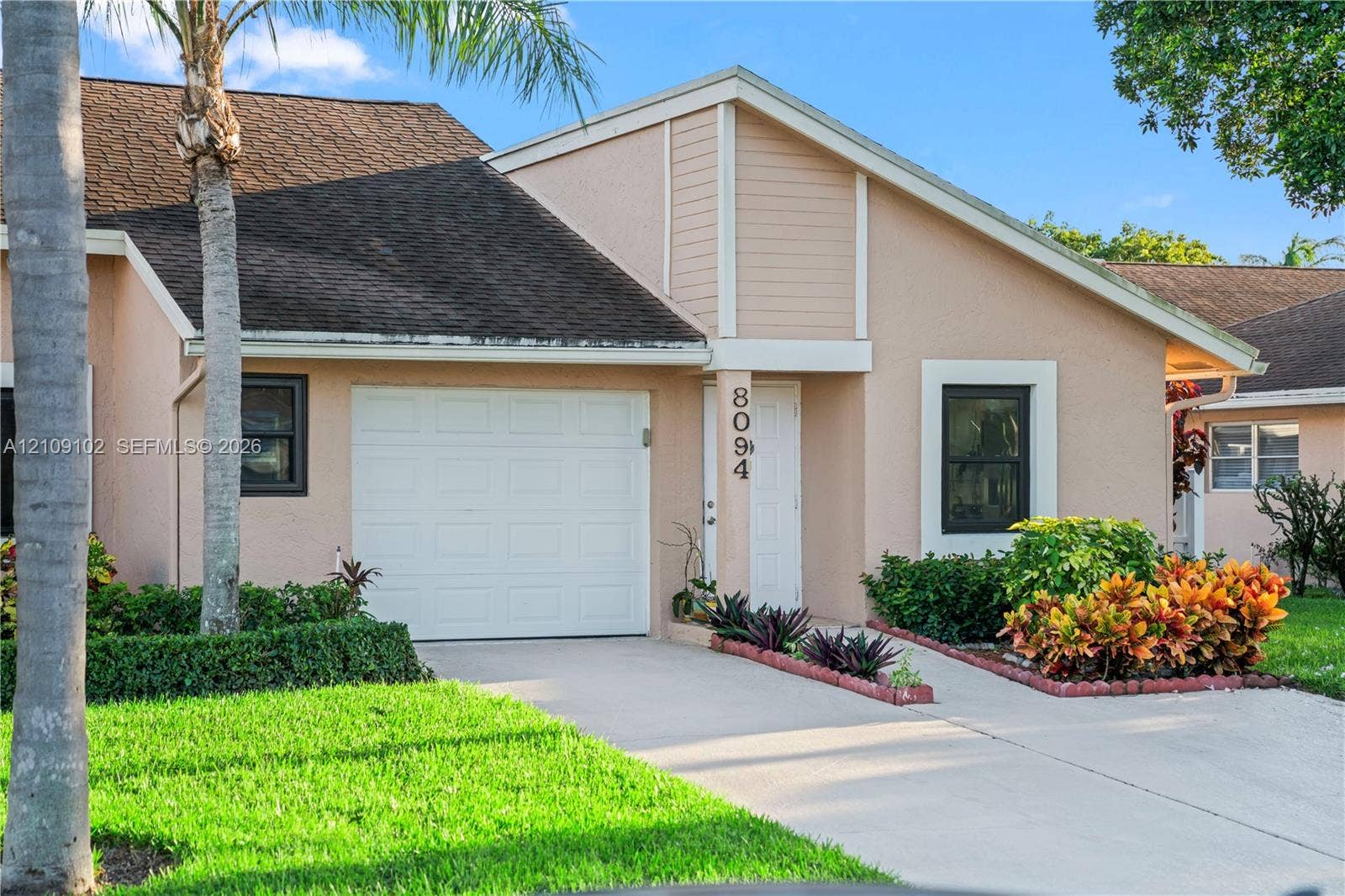 Stucco exterior featuring an attached one-car garage, concrete driveway, and landscaped garden beds