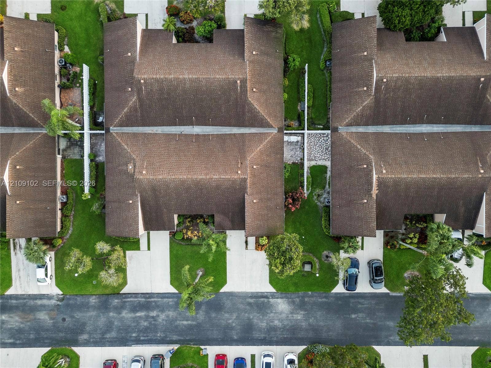 Aerial perspective featuring multi-unit structures with shingled roofs, paved driveways, established landscaping, and concrete walkways