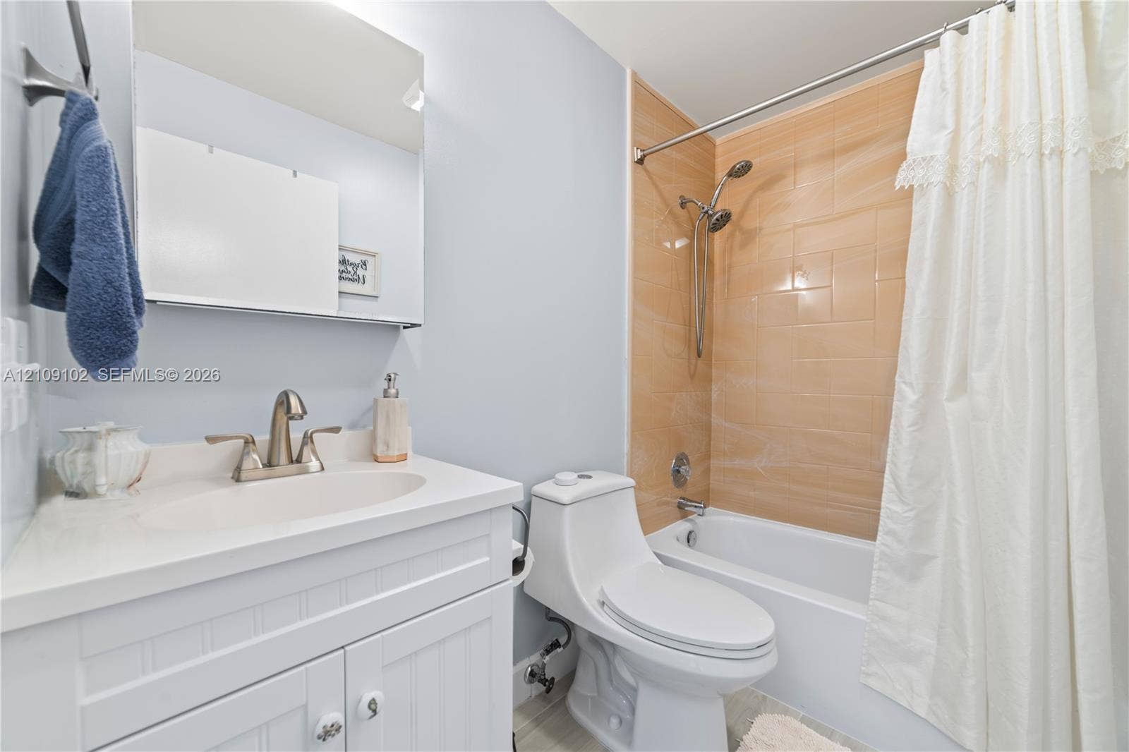 Bathroom featuring a white beadboard vanity with a solid-surface countertop, an integrated sink, a medicine cabinet, a dual-flush toilet, and a bathtub with a polished metallic shower fixture and light-toned tile surround