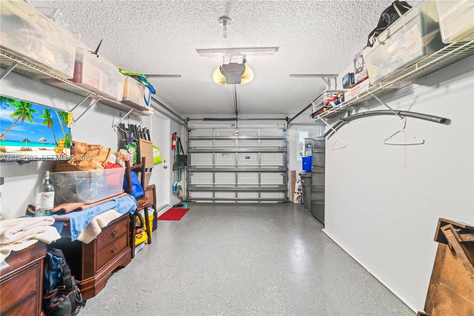 Enclosed garage featuring a sectional overhead door, epoxy-coated flooring, and overhead wire shelving units