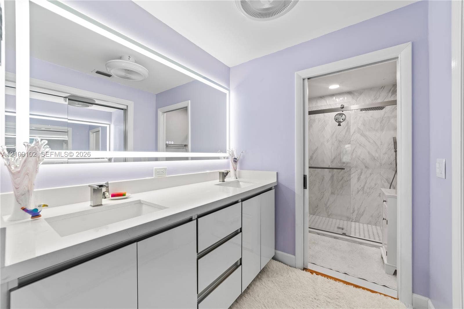 Double vanity with integrated sinks, quartz-finish countertop, full-width backlit mirror, and gloss-finish cabinetry