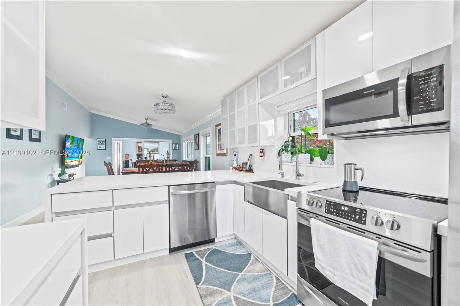 Kitchen featuring white cabinetry with glass-panel upper doors, stainless steel farmhouse sink, quartz-style countertops, and stainless steel appliances