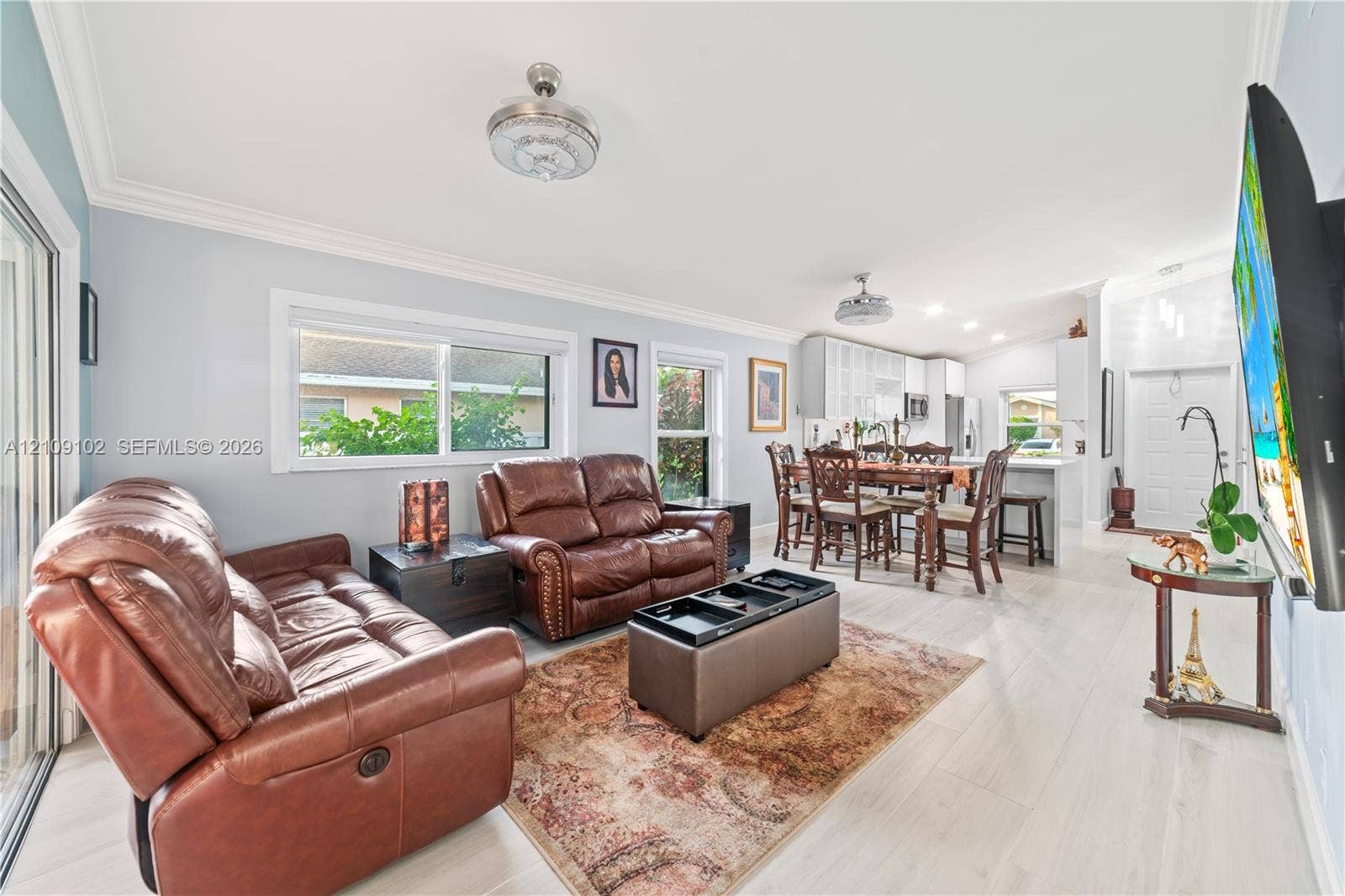 Open-concept living space featuring wood-finish flooring, recessed lighting, crown molding, dual ceiling fans, and sliding glass door access