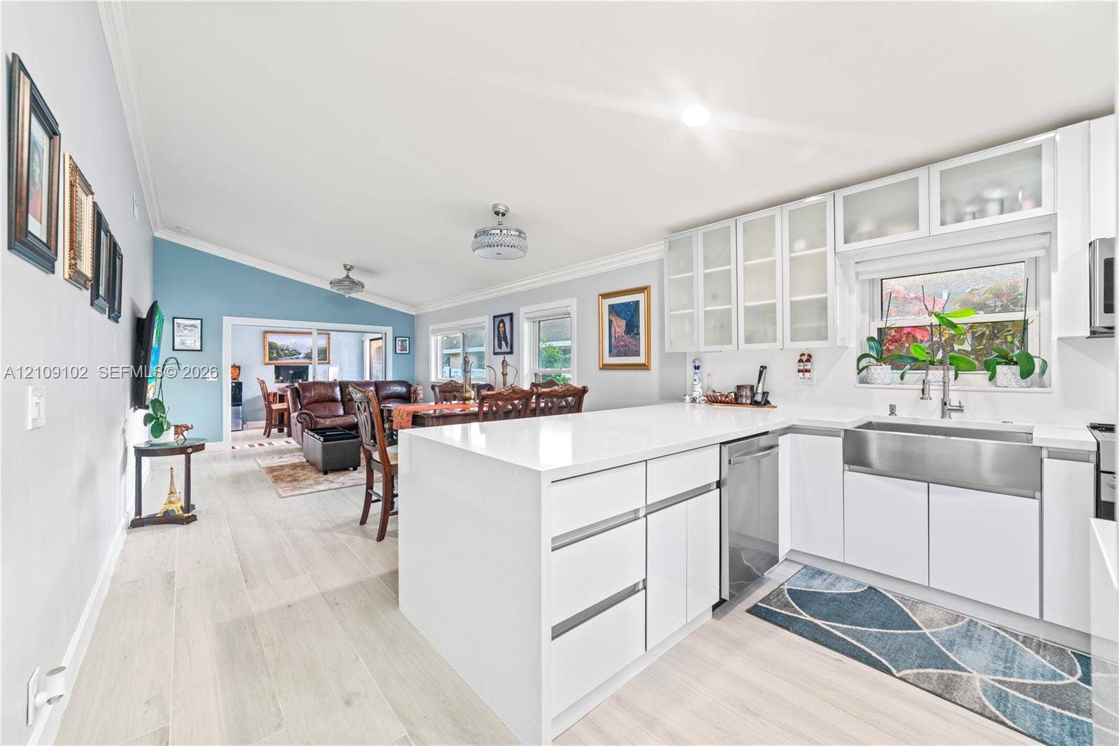 Kitchen featuring a solid surface peninsula, white flat-panel cabinetry with glass-front uppers, stainless steel apron-front sink, and wood-finish flooring