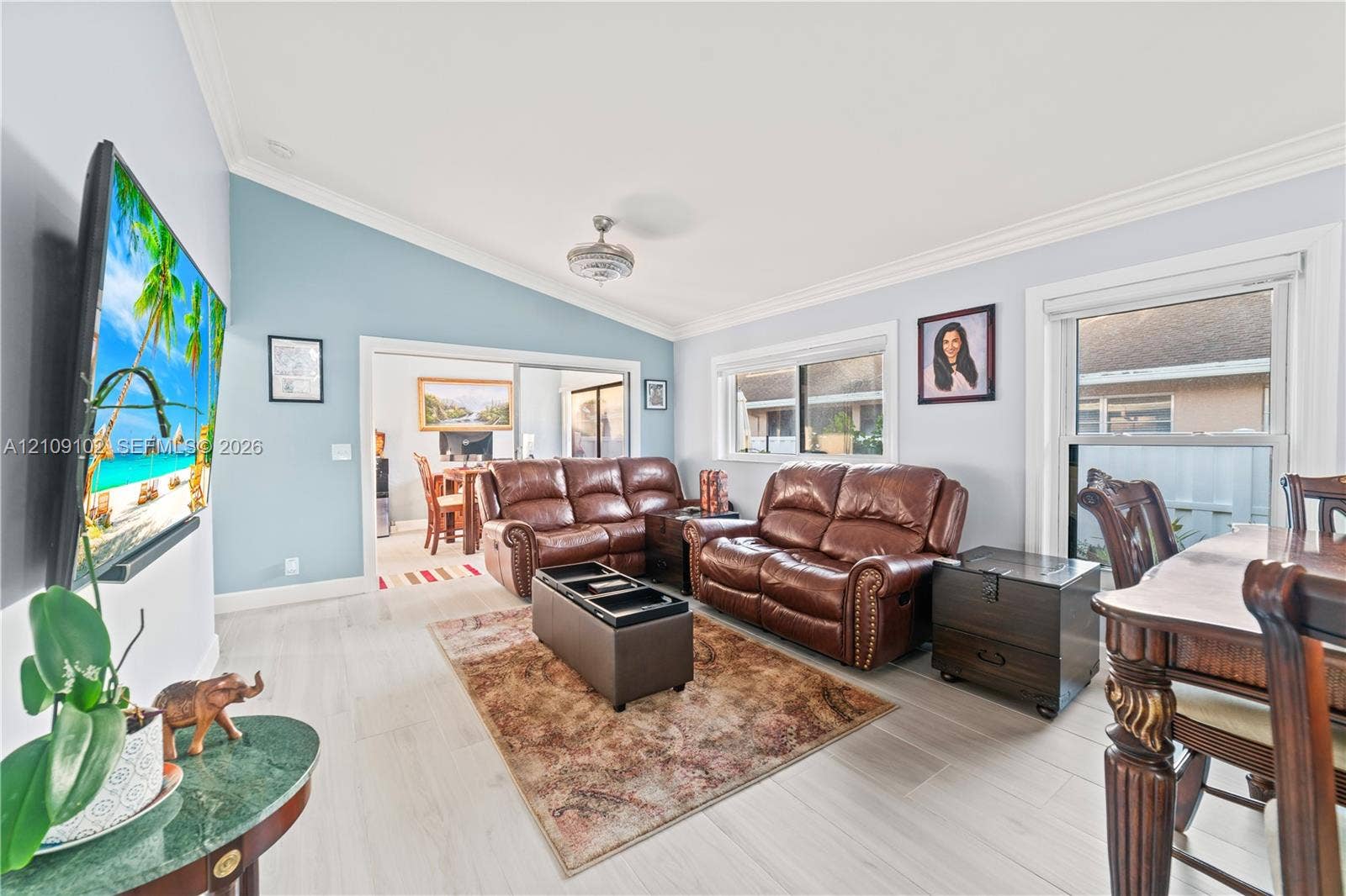 Vaulted ceilings with crown molding, wood-finish flooring, and natural lighting provided by large windows
