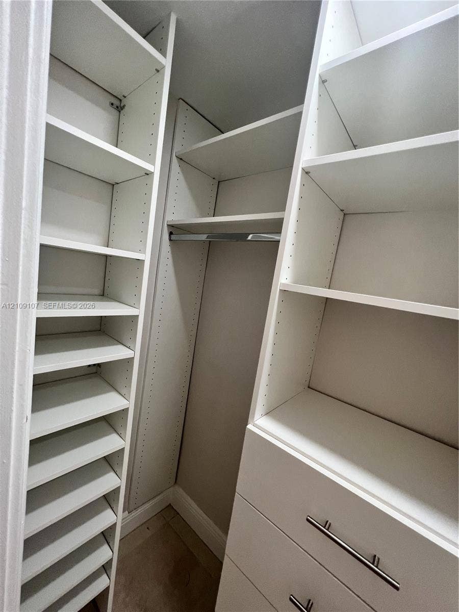 Walk-in closet featuring white built-in shelving, adjustable storage racks, a metal hanging rod, and drawers with metallic bar pulls