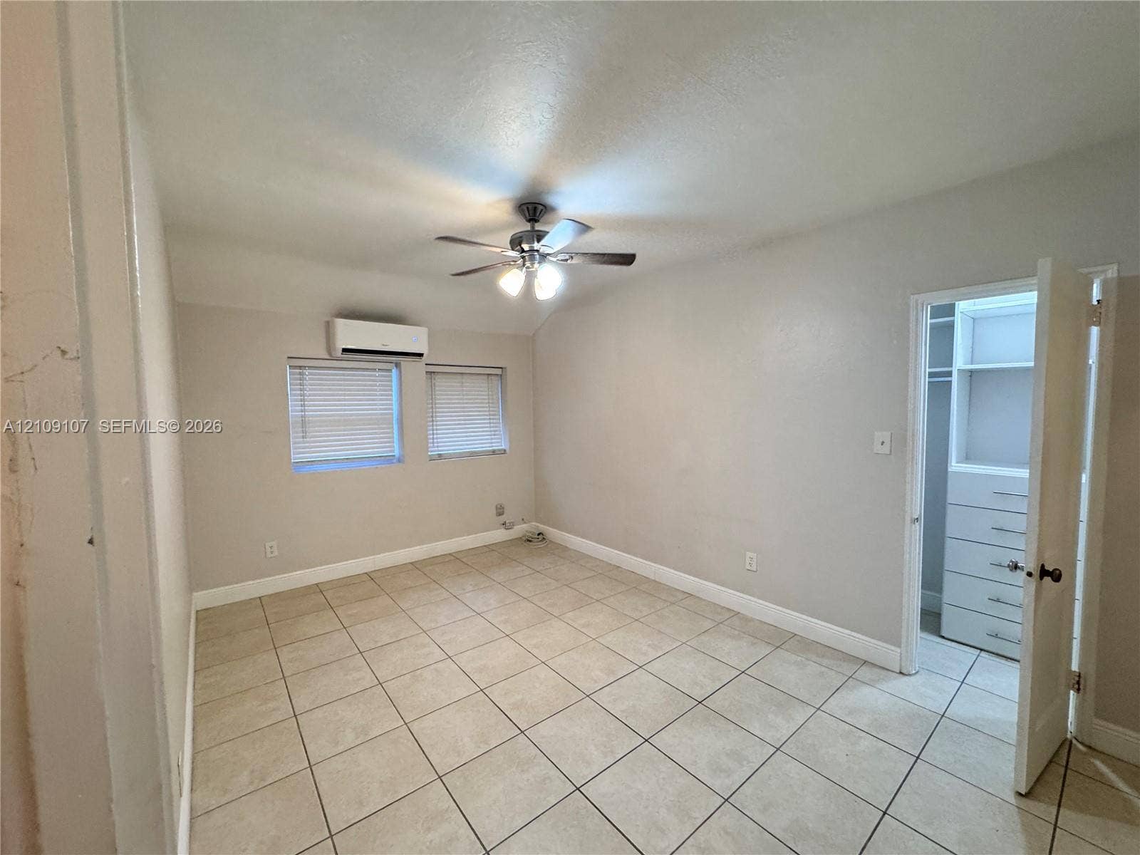 Room featuring ceramic tile flooring, a mounted ductless mini-split system, ceiling fan with light fixture, and walk-in closet with built-in shelving and drawer units