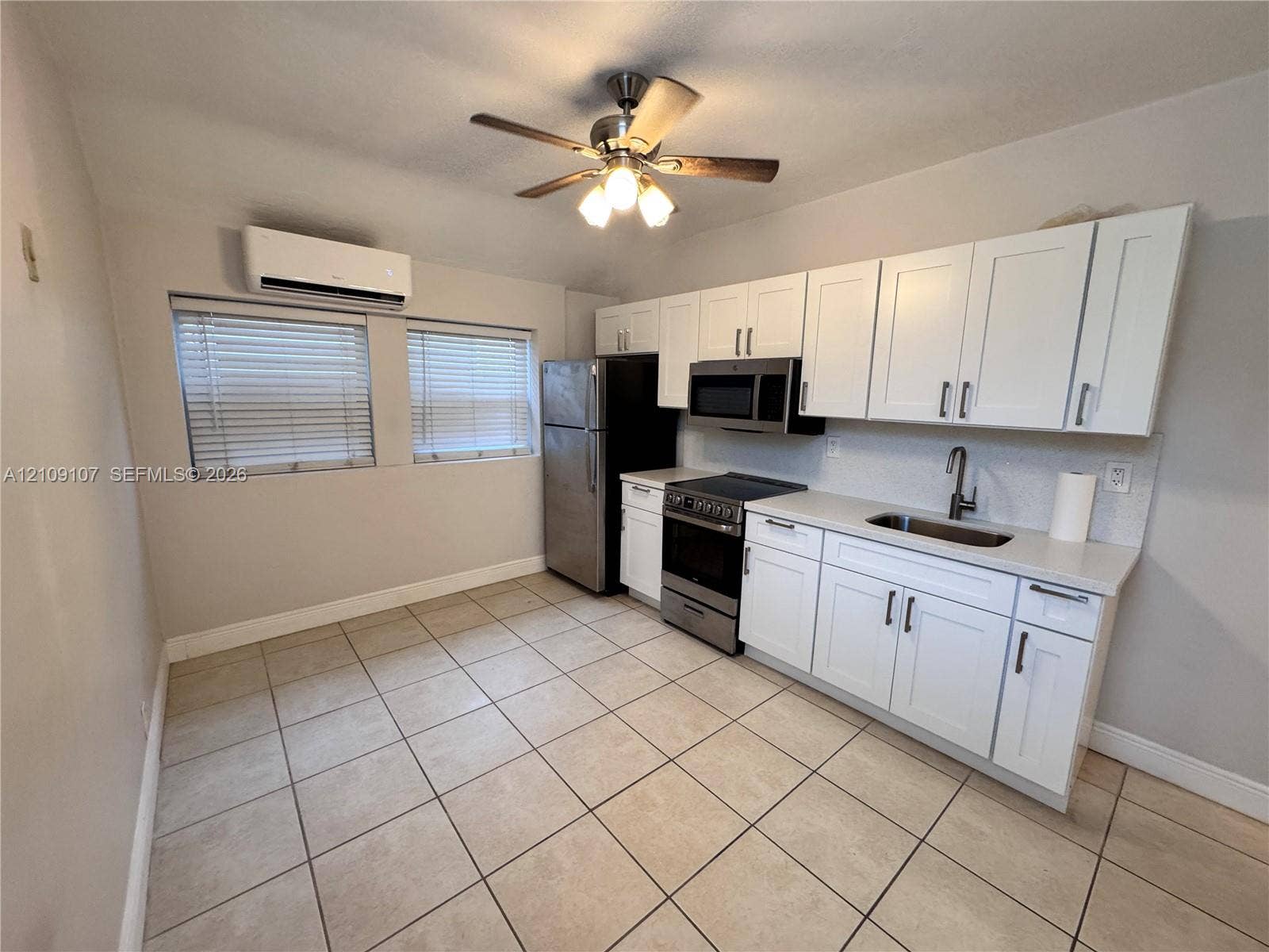 Kitchen featuring white shaker-style cabinetry, stainless steel appliances, tile flooring, and a wall-mounted ductless climate control unit