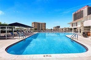 Swimming pool featuring a stone-paver deck, metal handrails, and a covered pavilion