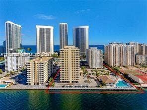 Waterfront high-rise property featuring an outdoor swimming pool, paved parking areas, and manicured landscaping