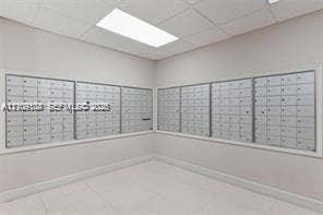 Secure metal mail center featuring a high-density, multi-compartment wall-mounted unit with recessed drop-ceiling lighting and neutral tile flooring