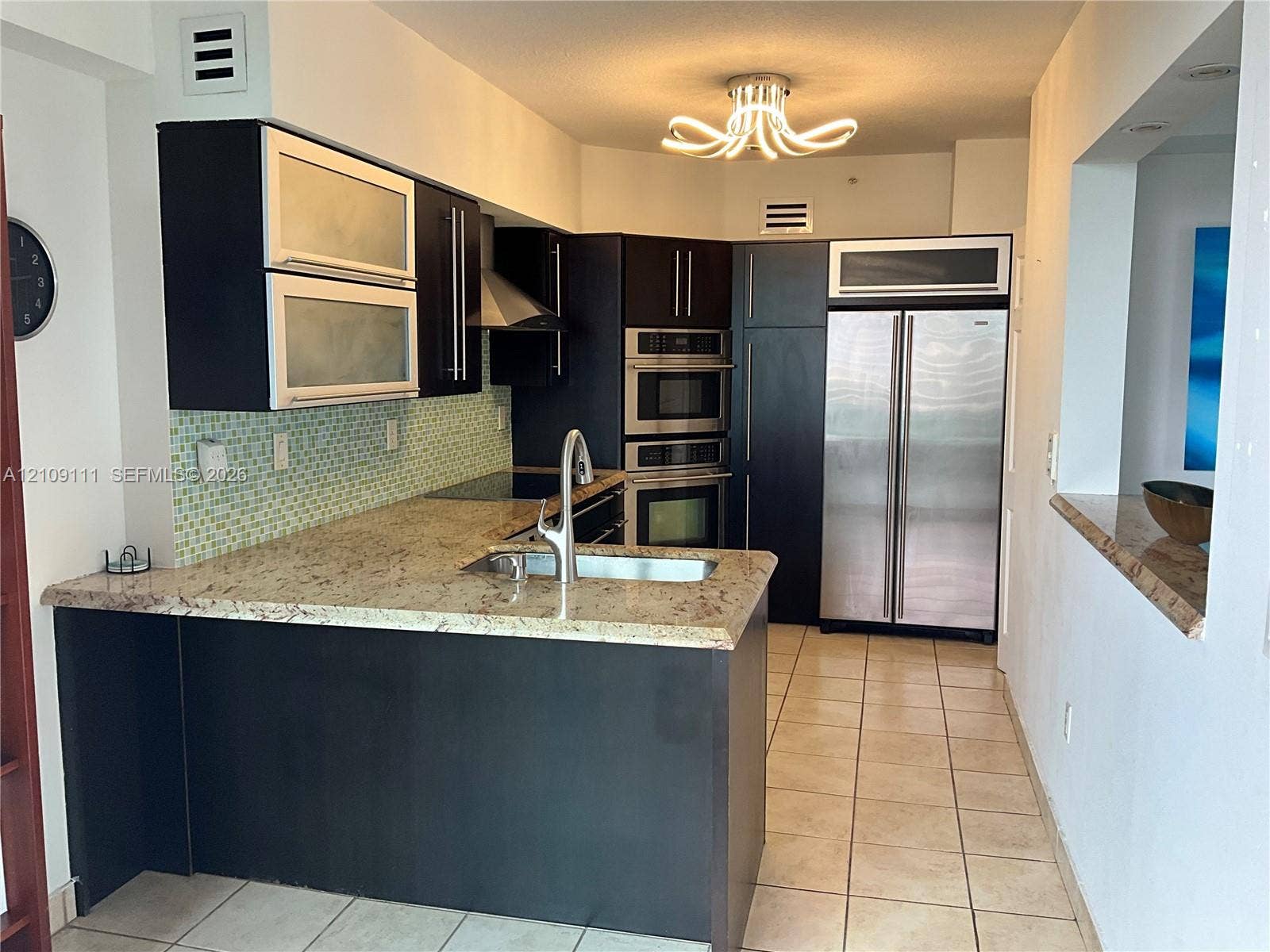 3370 Hidden Bay Drive, #801, Aventura, FL 33180 Kitchen featuring dark cabinetry, stone countertops, a mosaic tile backsplash, built-in stainless steel appliances, and a peninsula with a stainless steel sink