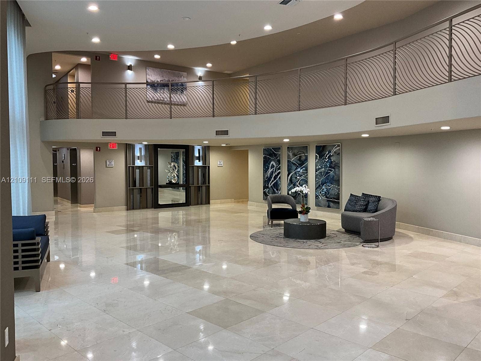 3370 Hidden Bay Drive, #801, Aventura, FL 33180 Double-height foyer featuring polished stone flooring, a curved mezzanine with decorative metal railing, recessed ceiling lighting, and built-in wall paneling