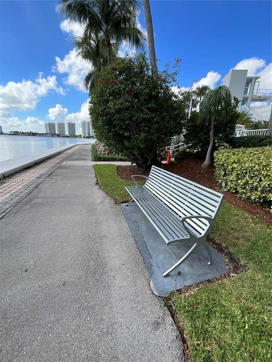 3370 Hidden Bay Drive, #801, Aventura, FL 33180 Waterfront promenade featuring a paved walking path, concrete bulkhead, mature palms, and metal outdoor seating