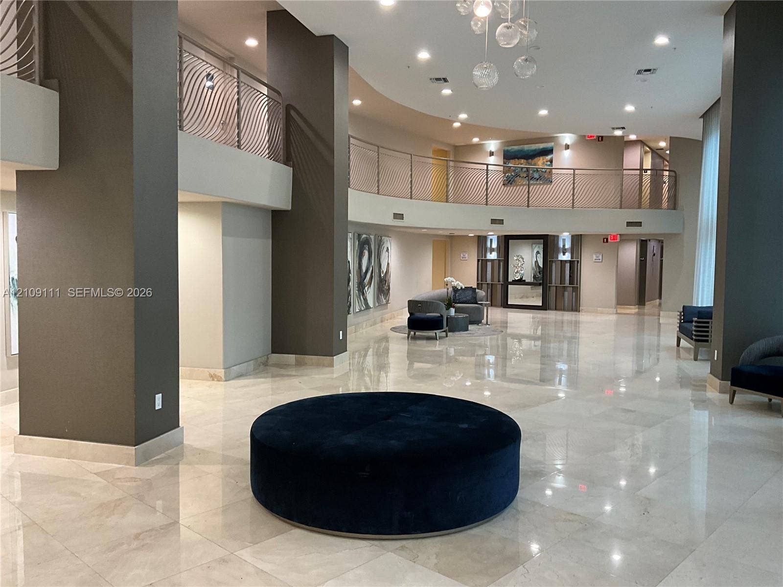 3370 Hidden Bay Drive, #801, Aventura, FL 33180 Grand lobby featuring polished stone flooring, a multi-story mezzanine with decorative metal railings, recessed lighting, and a modern glass chandelier