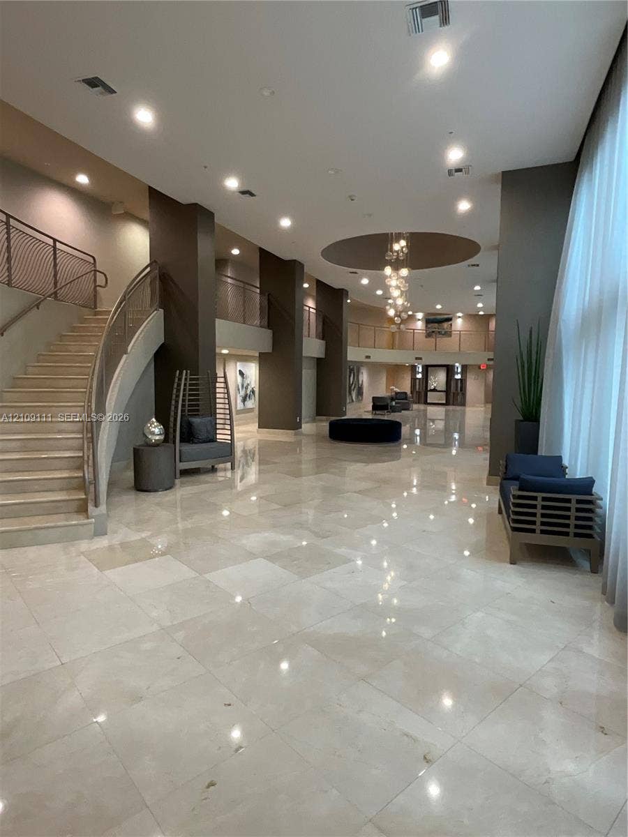 3370 Hidden Bay Drive, #801, Aventura, FL 33180 Grand entrance hall featuring high ceilings, stone tile flooring, a multi-tiered glass chandelier, a sweeping staircase with custom metal railings, and a tiered mezzanine level